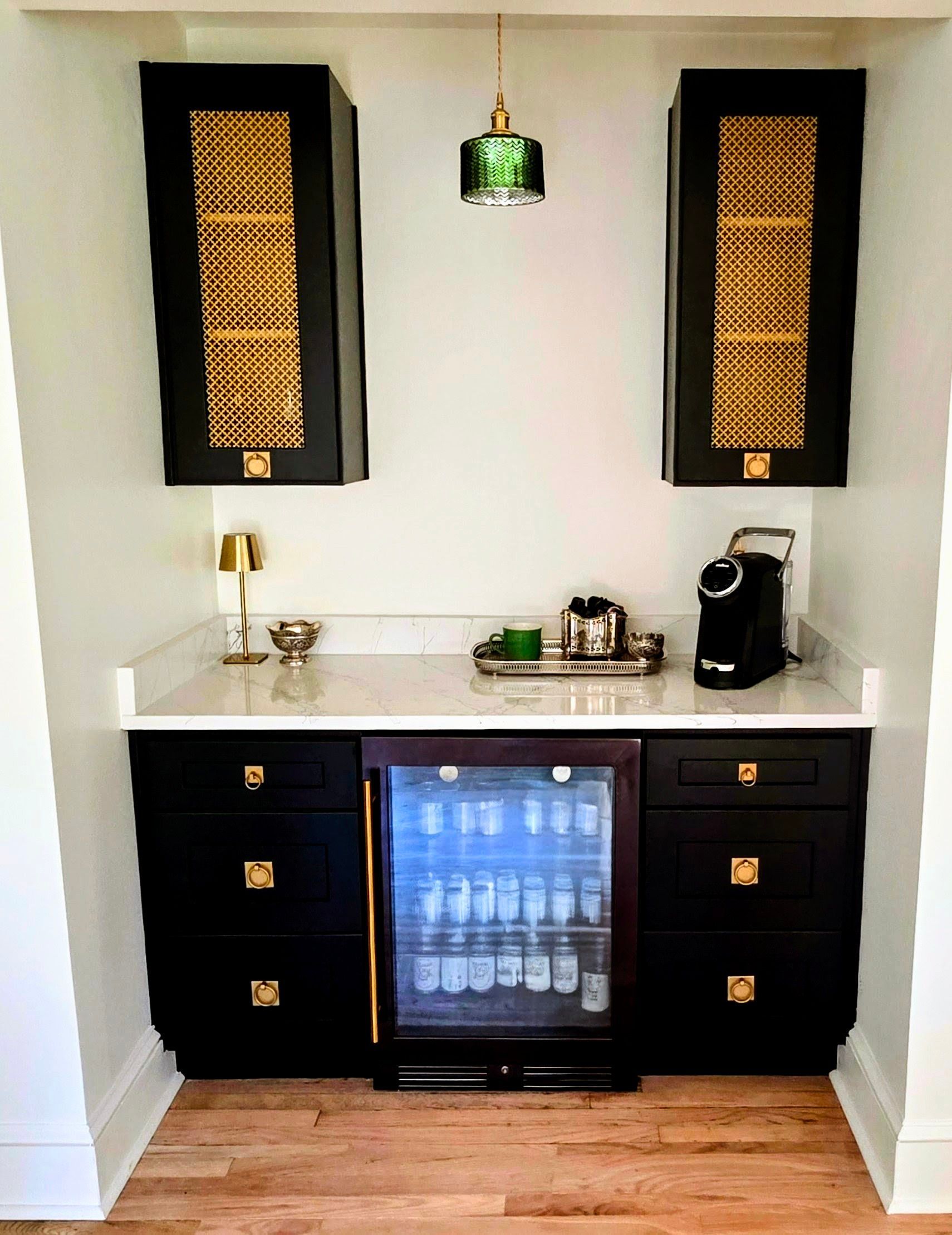 Built-in black bar cabinet with gold accents, white countertop, mini-fridge, and hanging green light.