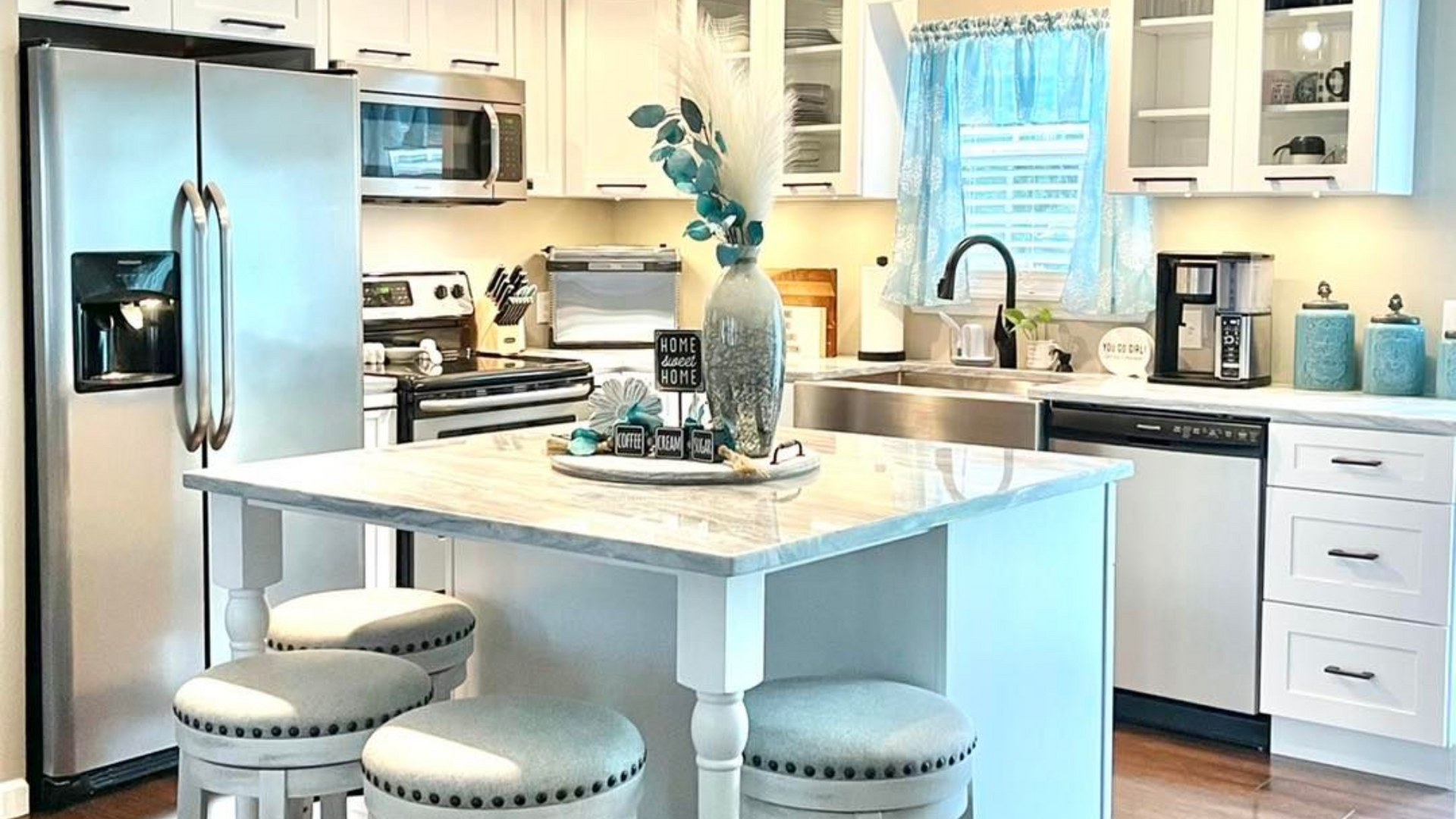 White kitchen with island seating, stainless steel appliances, and light blue accents.