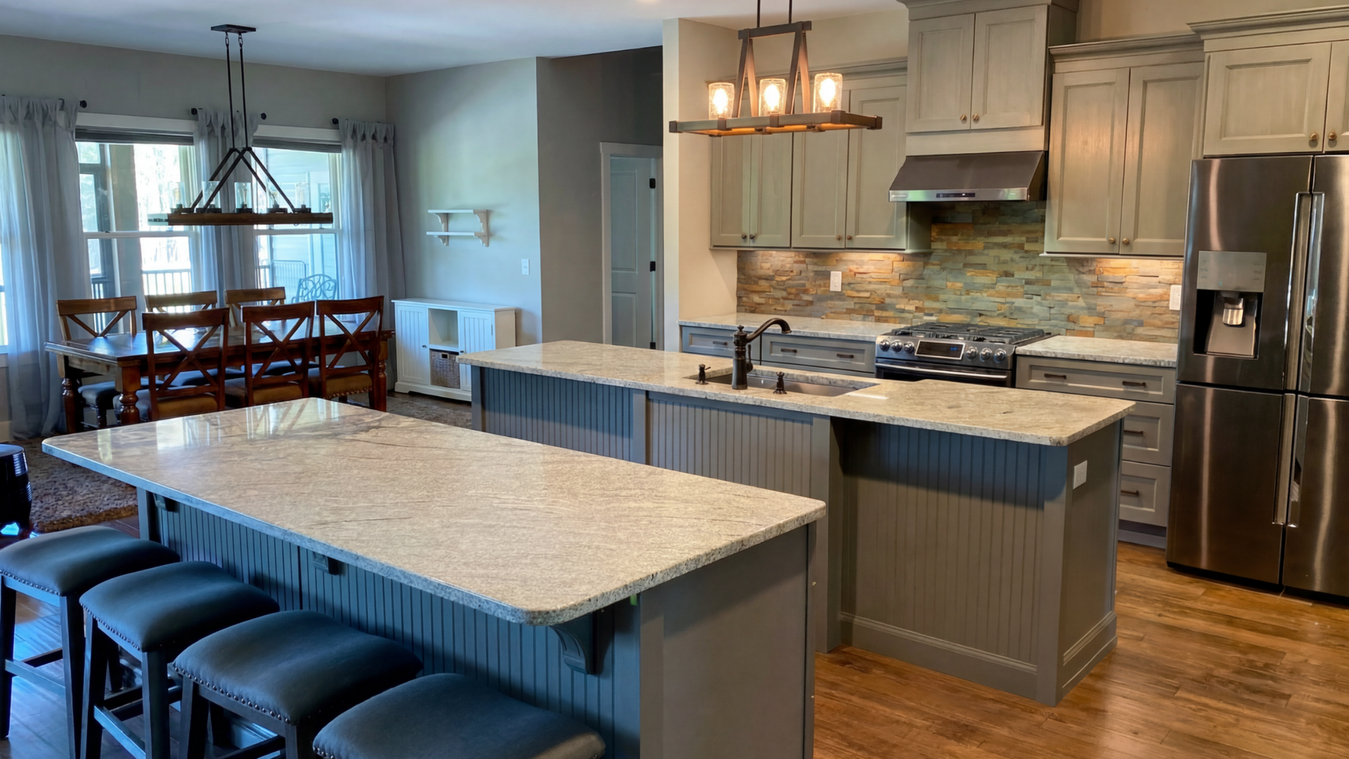 Modern open kitchen with island, pendant lights, stainless appliances, and dining area beyond.
