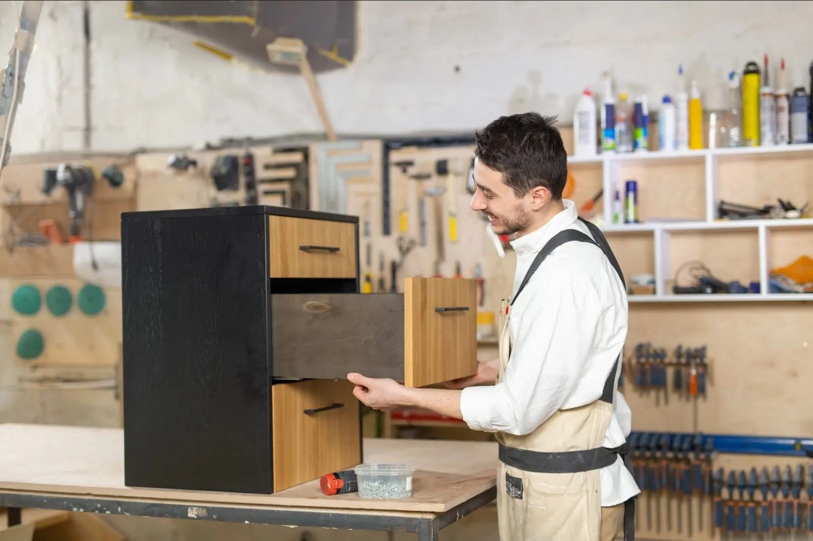 A man is working on a wooden cabinet in a workshop.