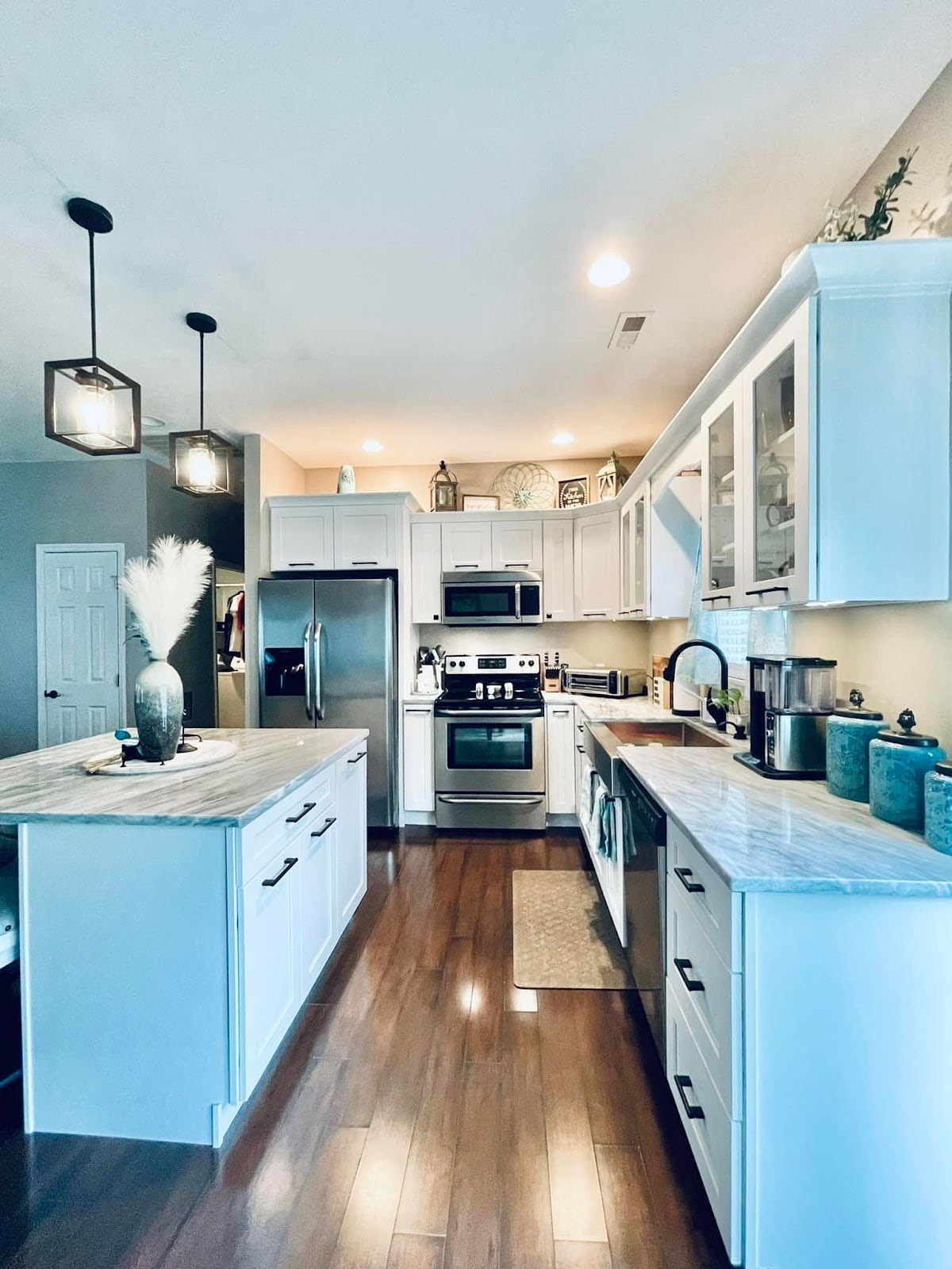 Bright kitchen with white cabinets, stainless steel appliances, and island with granite countertop.