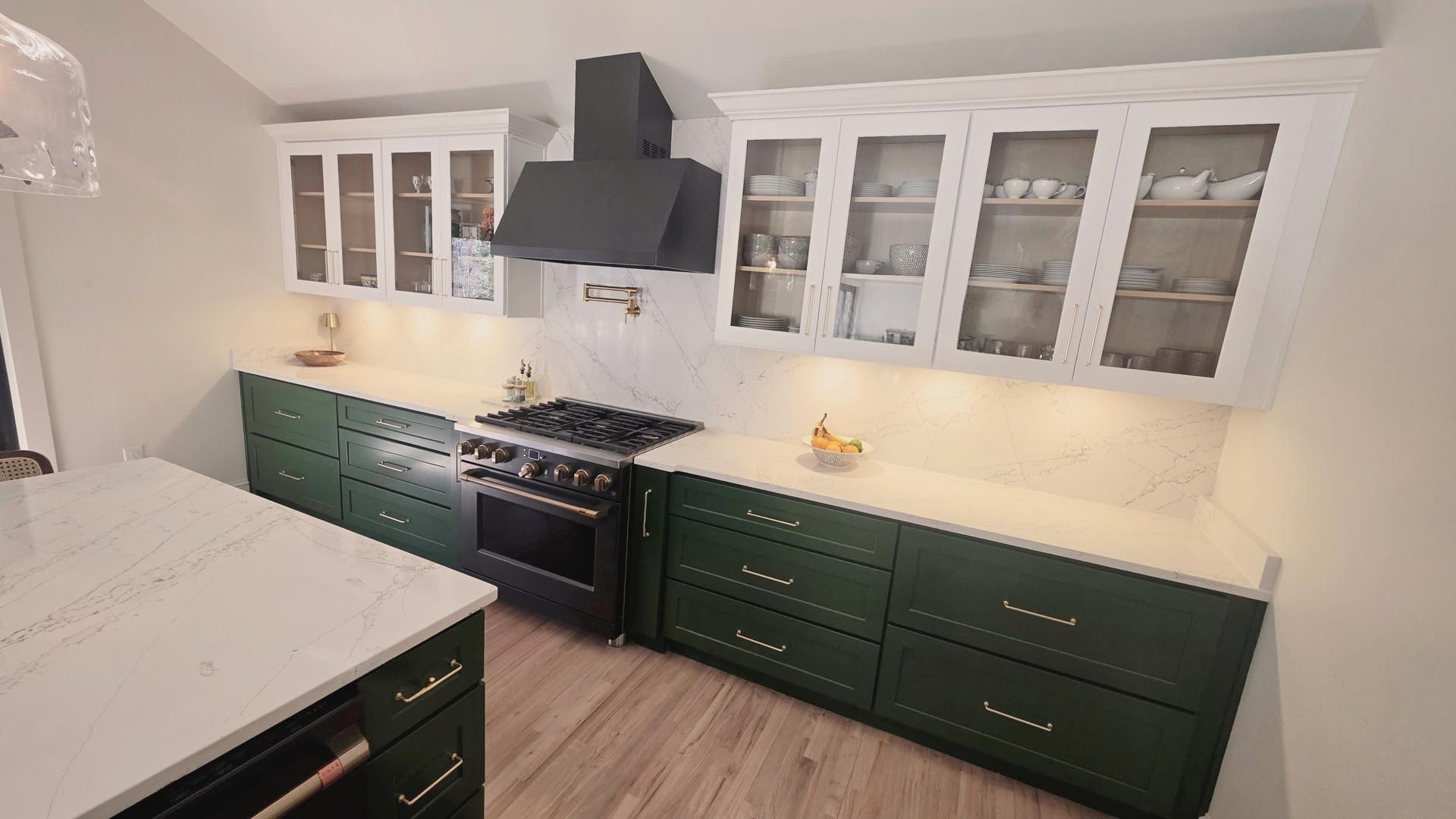 Bright kitchen with green cabinets, white countertops, glass-front upper cabinets, and a black stove.
