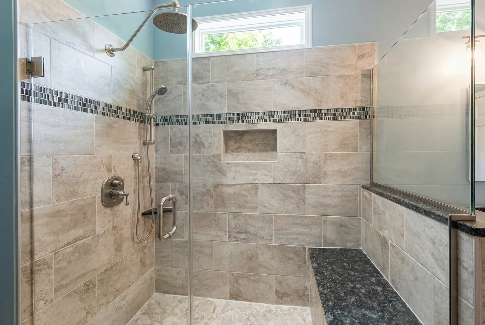 Tiled shower with glass door and bench seat, silver fixtures, blue walls, and a decorative tile band.