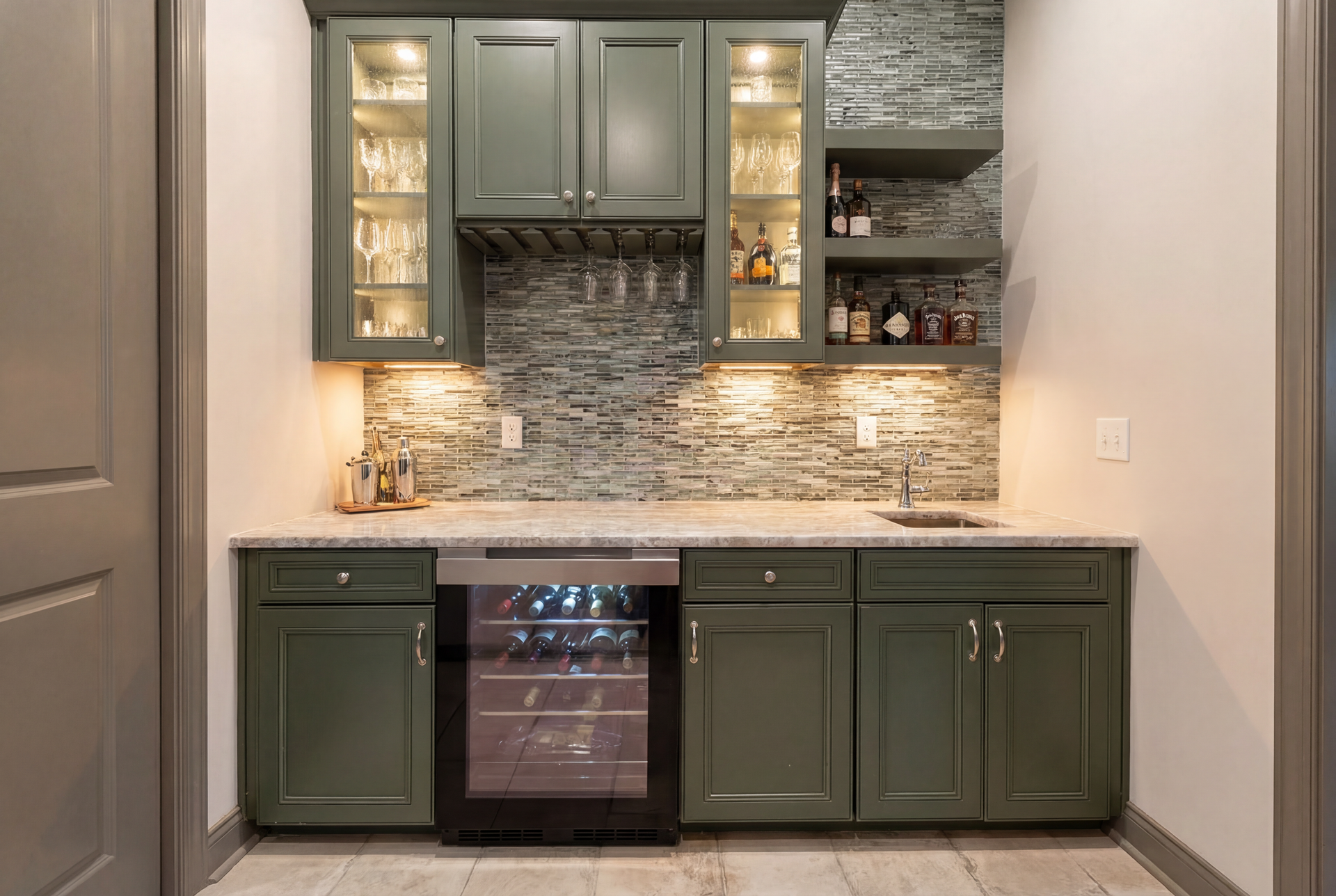 Green home bar with wine cooler, cabinets, glass rack, and shelves. Stone backsplash and countertop.