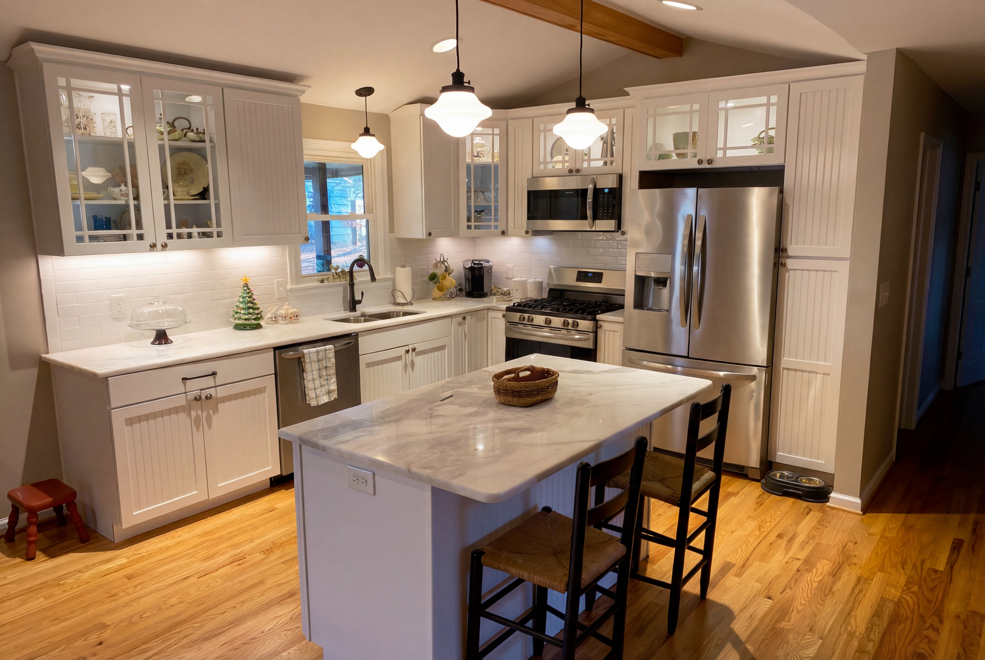 White kitchen with island and stainless steel appliances; hardwood floors.