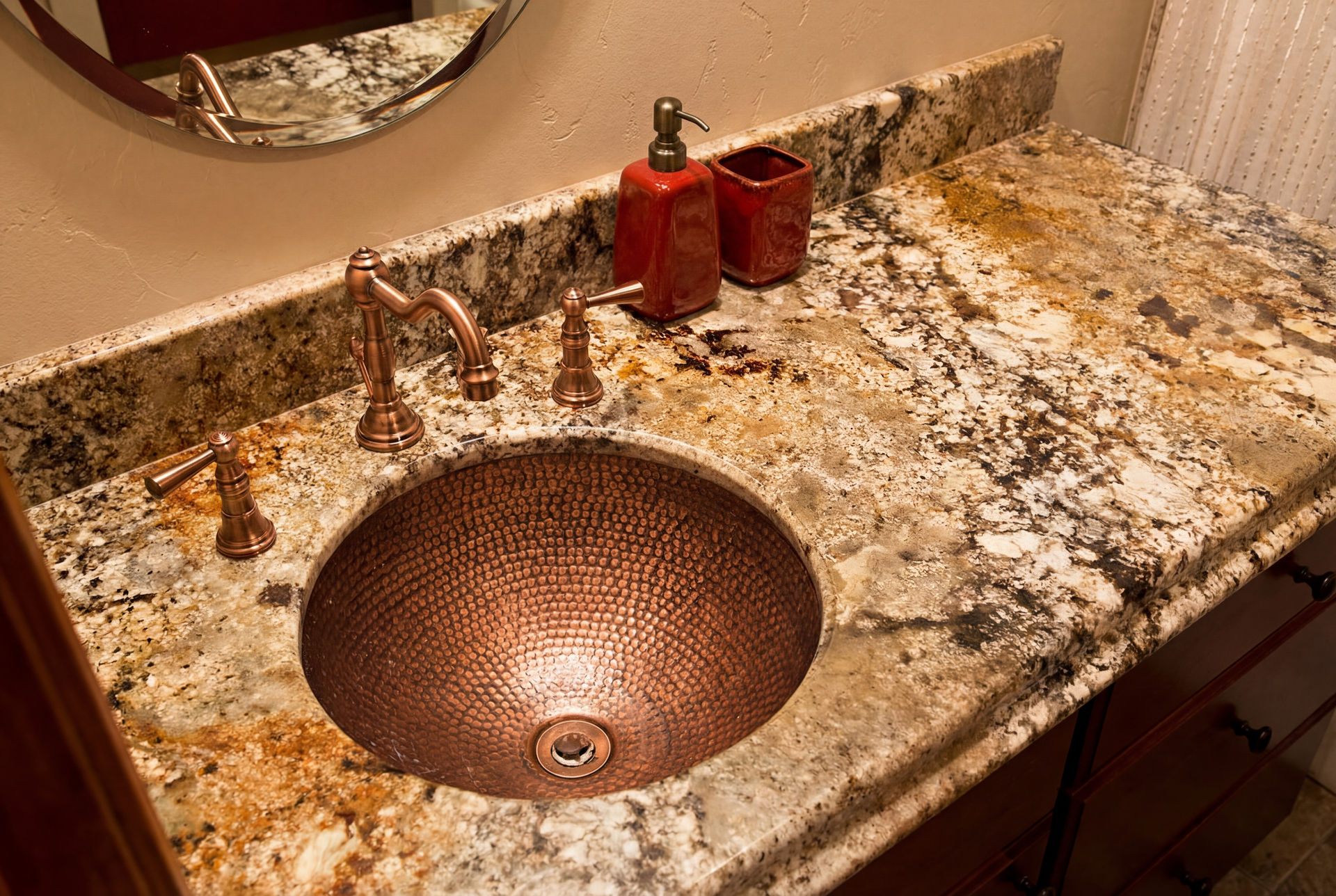 Copper sink and fixtures on a granite countertop, with soap dispenser and cup.