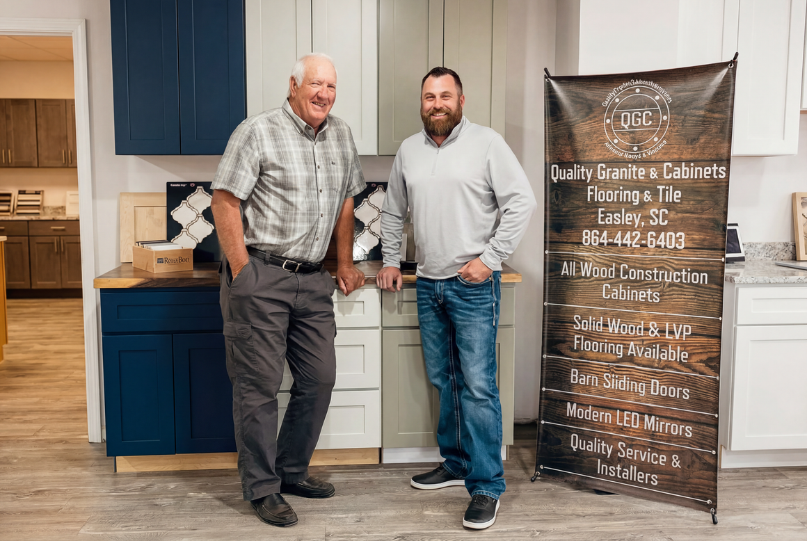 Two men stand beside cabinets; one has his hands in his pockets, the other leans on a cabinet, with a banner to their right.