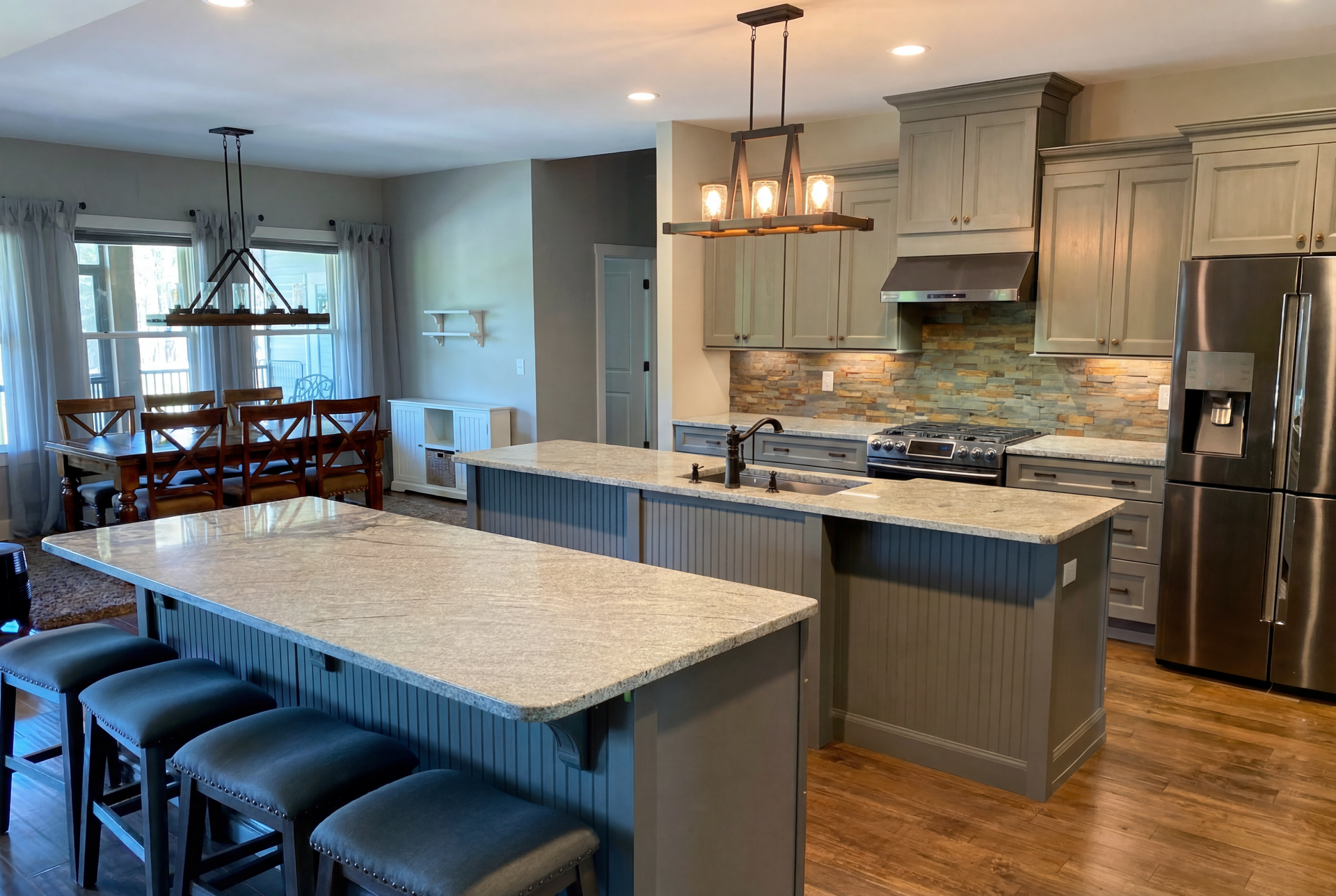Kitchen with two granite islands, gray cabinets, stainless steel appliances, and wood flooring.