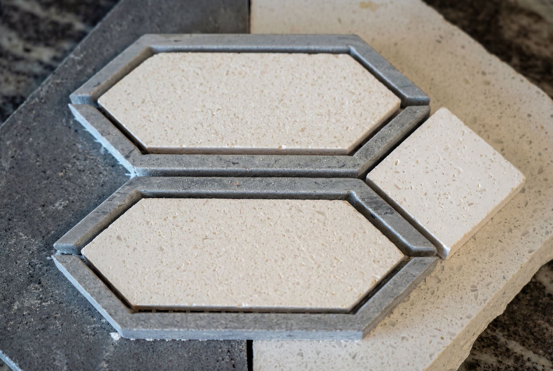 Two decorative stone tiles, white hexagon with gray border, and white square, on two other stone slabs.