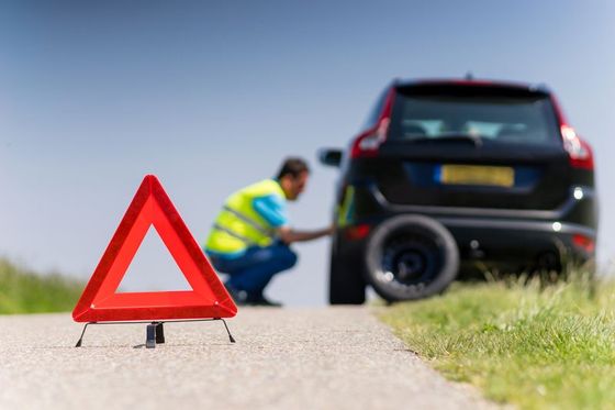 vista di un triangolo su un lato della strada e dietro un uomo con una pettorina giallo fosforescente intento nel sostituire la ruota