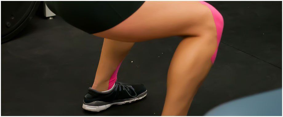 A woman is doing squats with pink kinesio tape on her leg