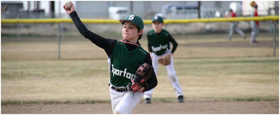A baseball player wearing a spartan jersey is throwing a ball