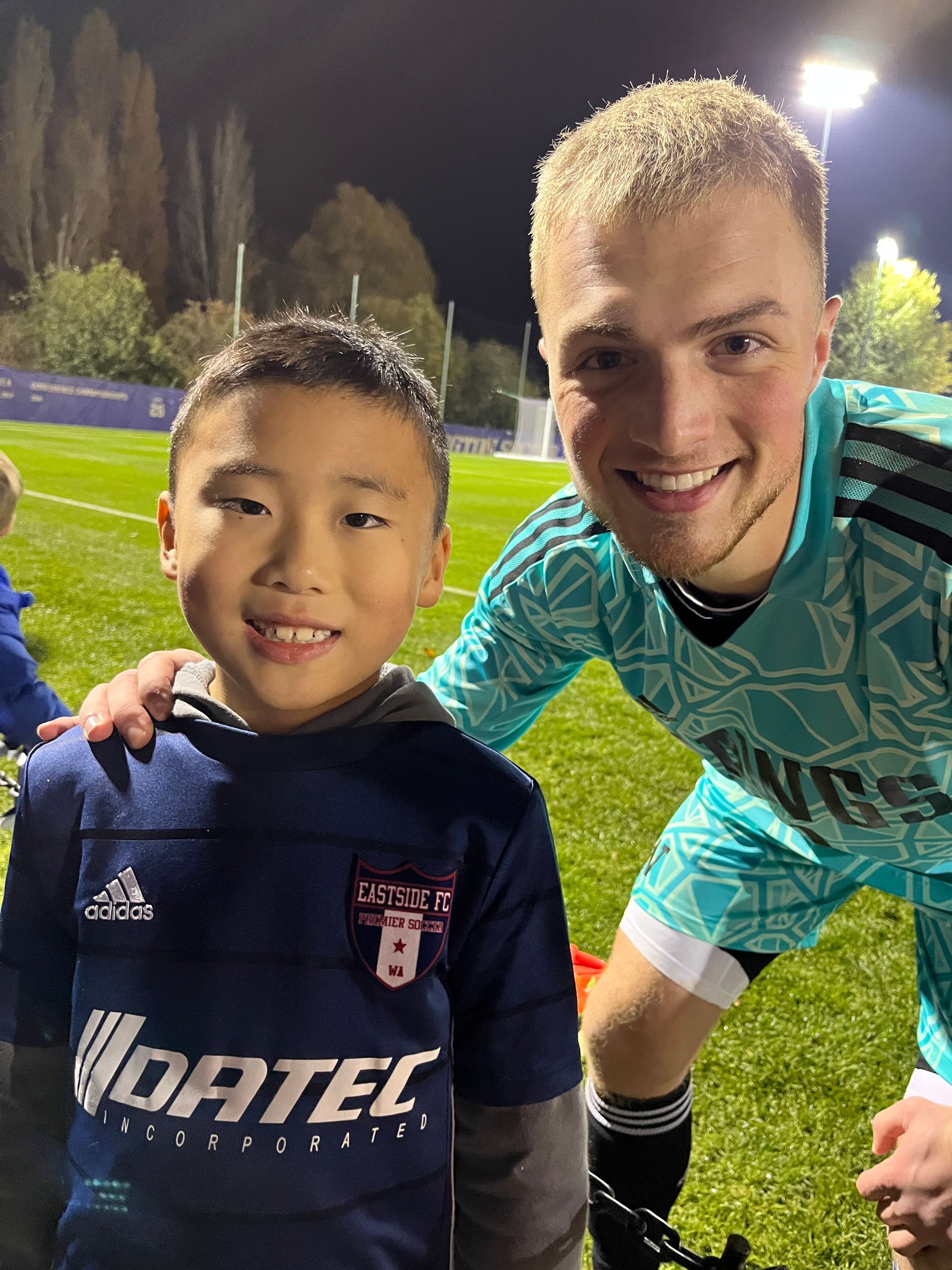 A man and a boy are posing for a picture on a soccer field.