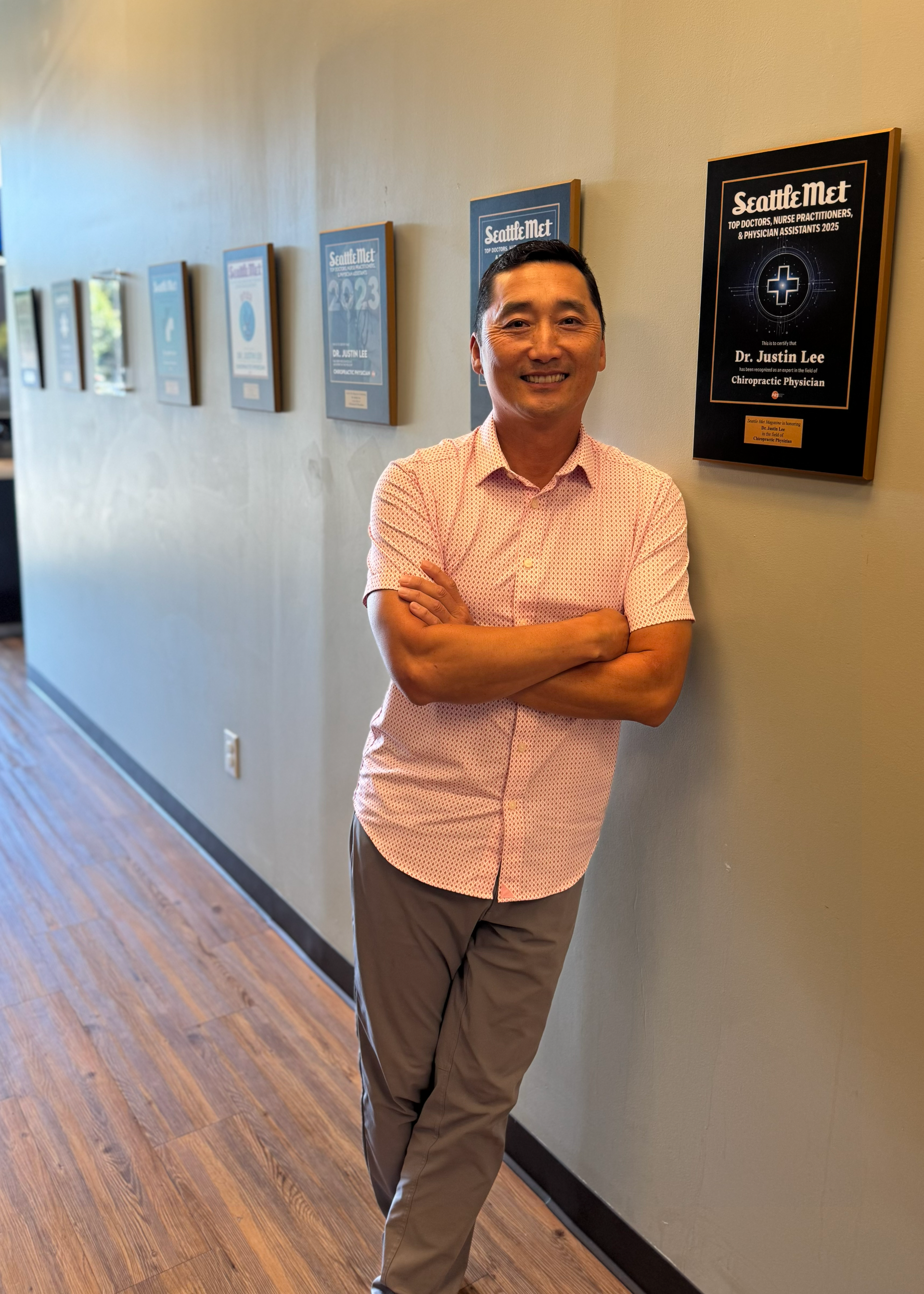 A man in a blue striped shirt is smiling in front of a brick wall.