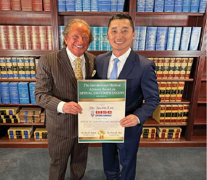 Two men standing next to each other in front of a bookshelf holding a certificate