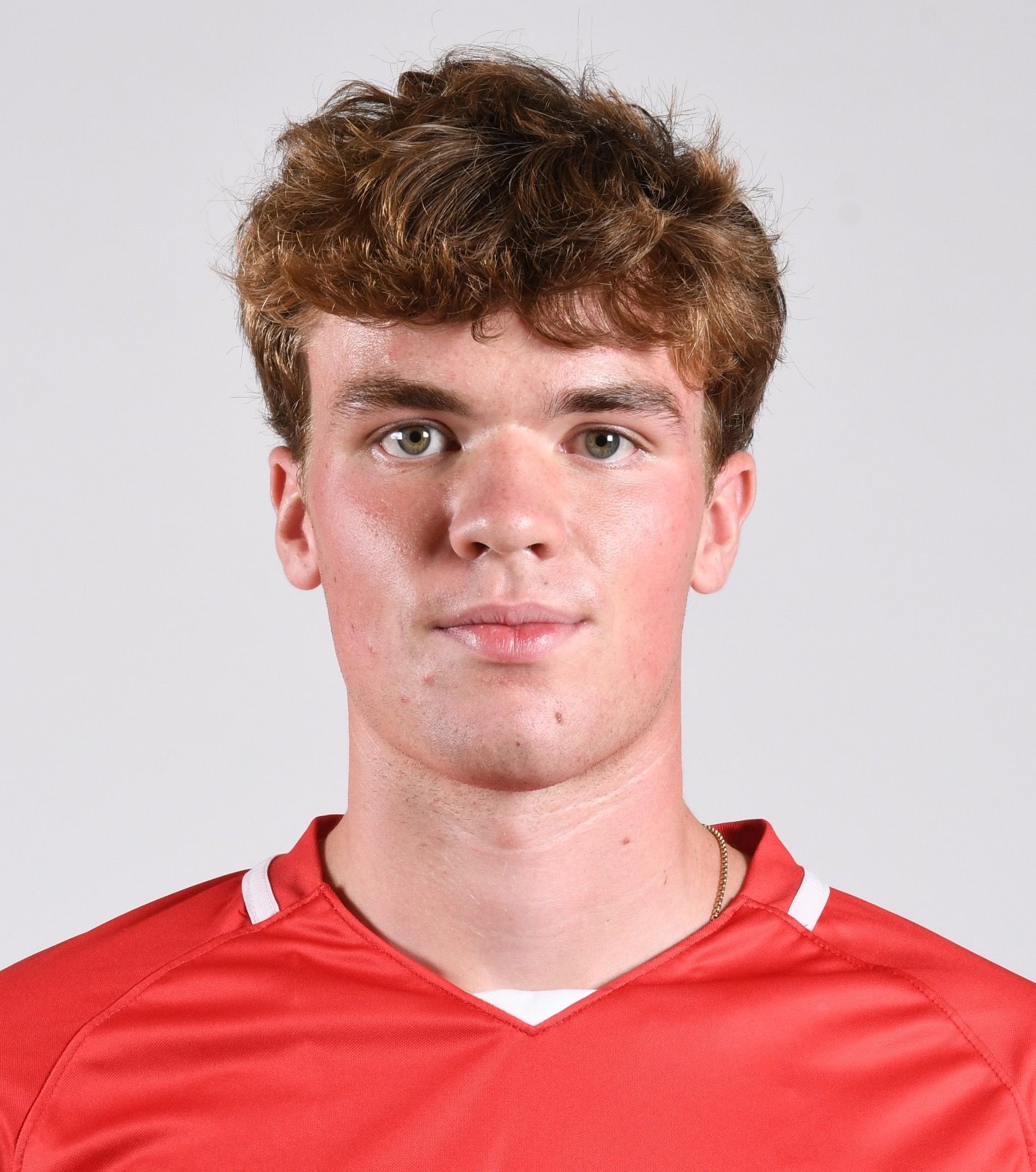 A young man in a red shirt is looking at the camera.