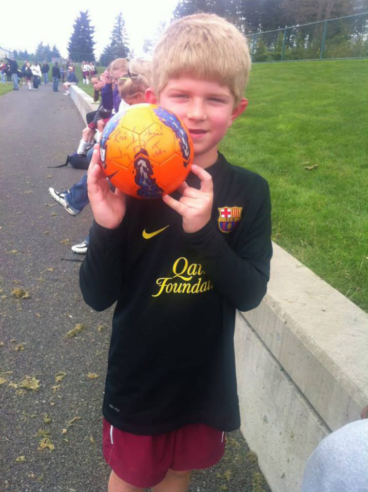 A boy wearing a qais founders shirt holds a soccer ball
