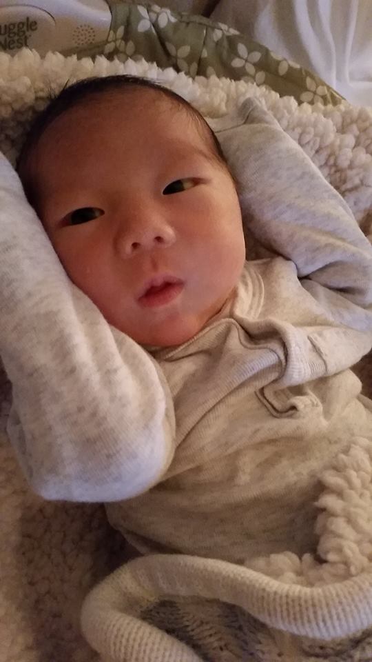 A newborn baby is laying on a blanket on a bed.