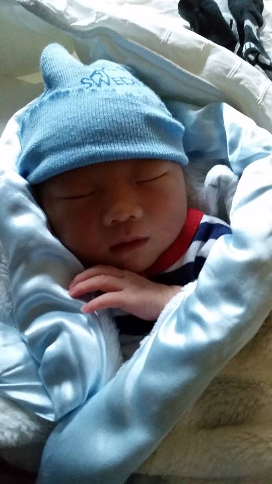 A newborn baby wearing a blue hat is wrapped in a blue blanket.