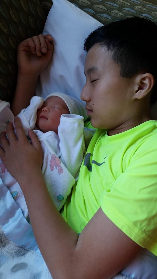 A young man is sleeping with a newborn baby.