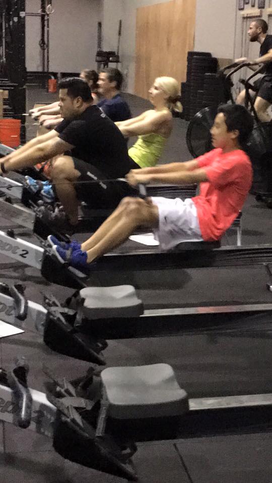 A group of people are doing exercises on rowing machines in a gym.