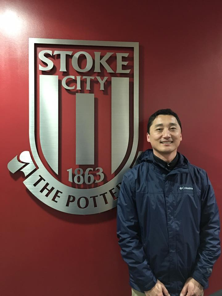 A man in a blue jacket is standing in front of a stoke city logo.