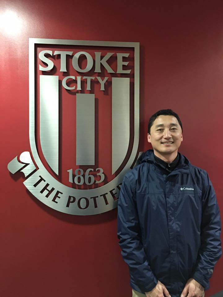 A man in a blue jacket is standing in front of a stoke city logo.