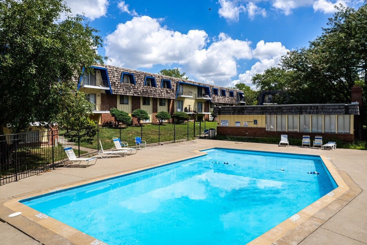 Swimming pool in front of apartment buildings on a sunny day with blue sky and some clouds.
