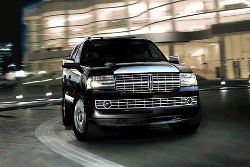 A black lincoln navigator is driving around a curve in front of a building at night.