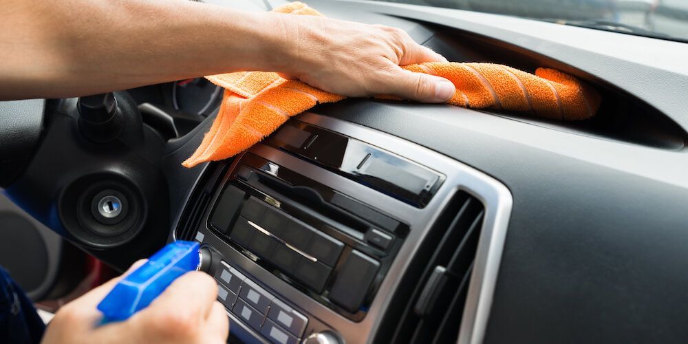 A person is cleaning the dashboard of a car with a cloth.