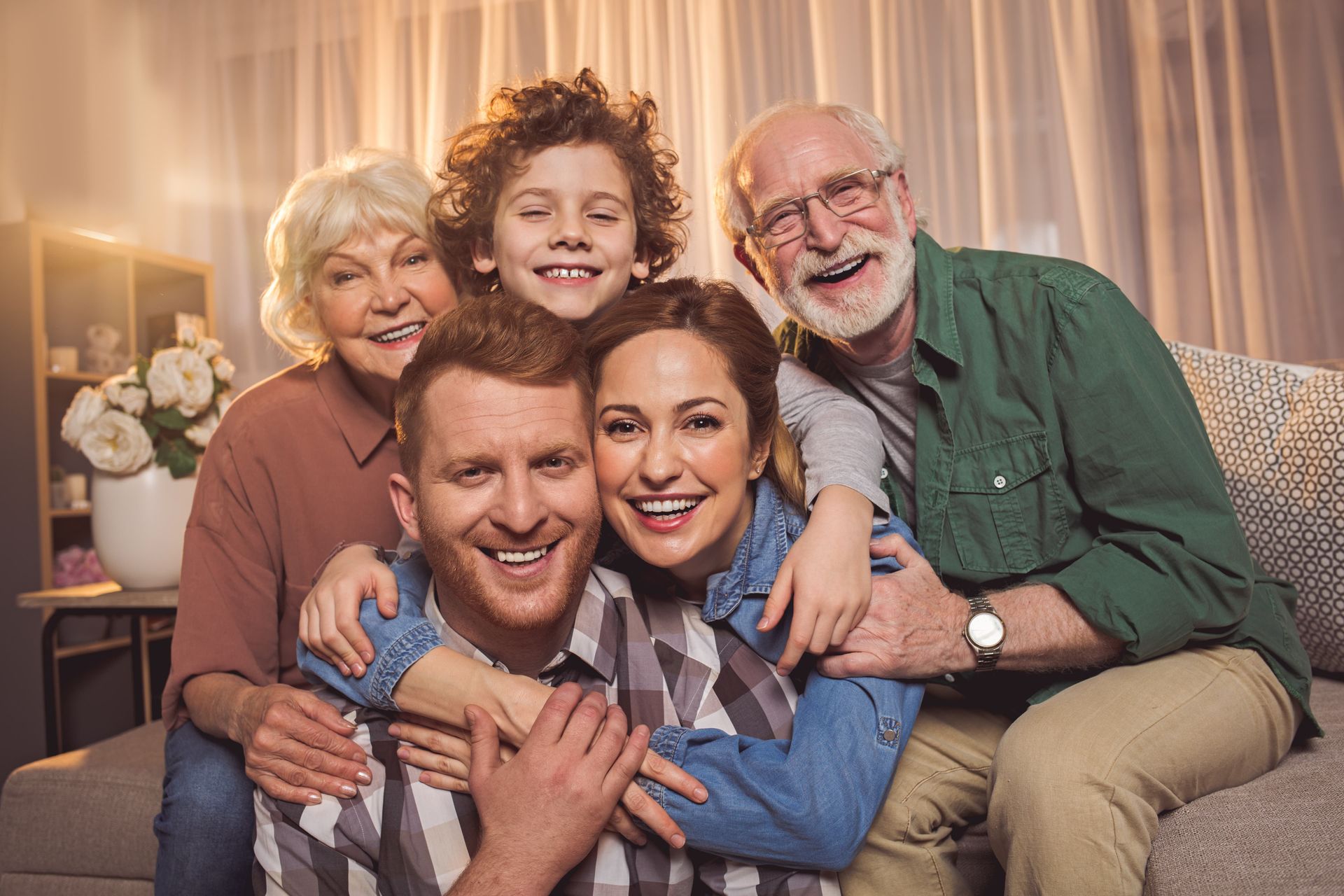 Family portrait, five smiling people in living room, including grandparents, parents, and child.