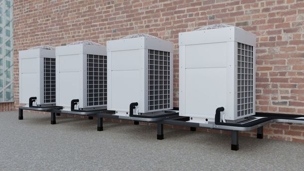 A row of air conditioners are sitting on the side of a brick building.