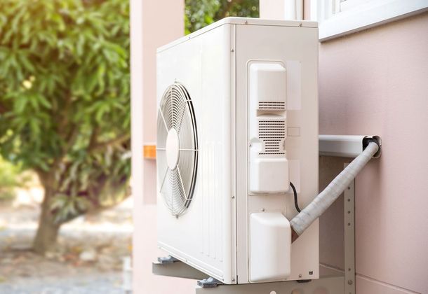 A white air conditioner is mounted on the side of a building.