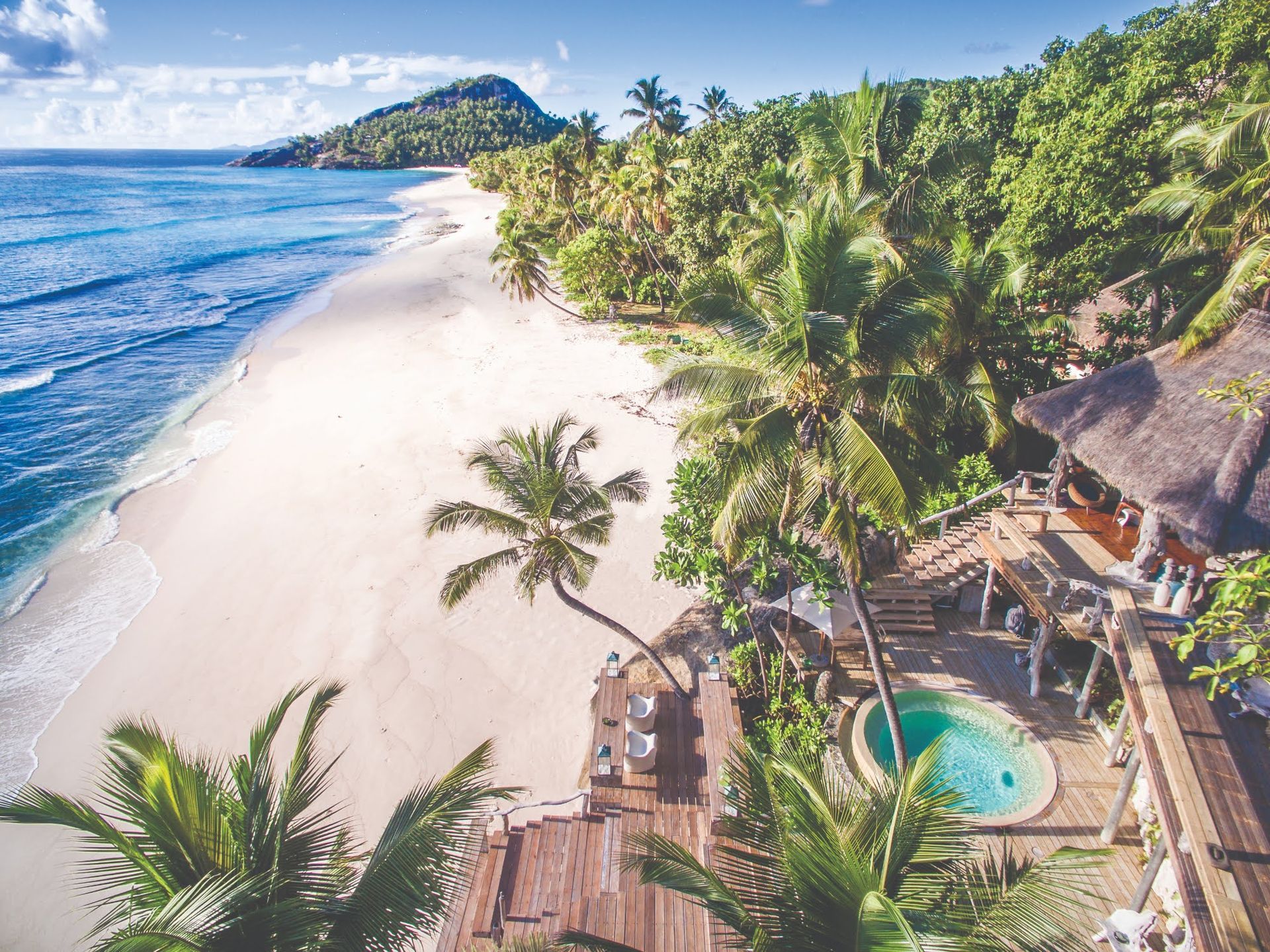 An aerial view of a tropical beach with palm trees and a swimming pool.