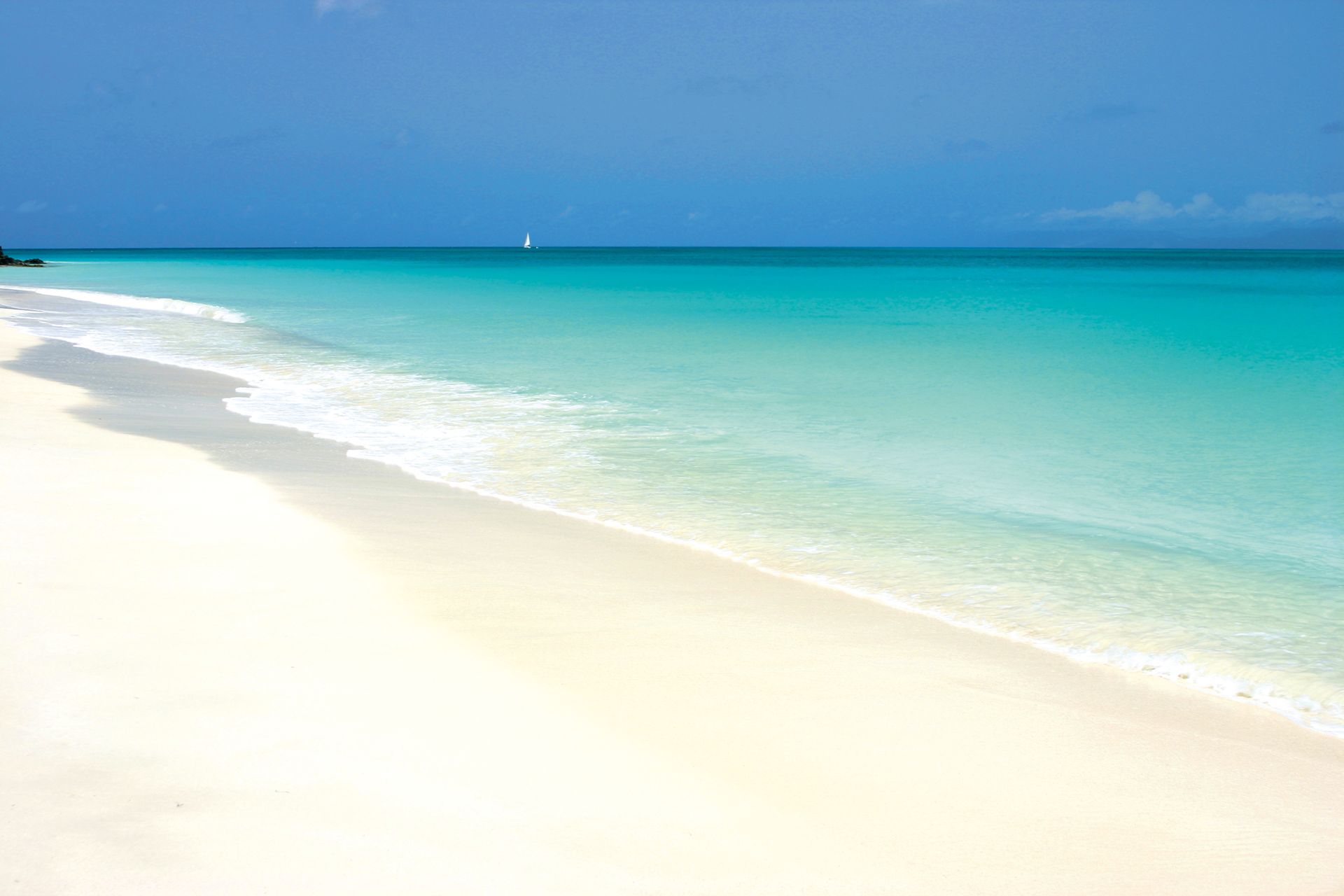 A white sandy beach with turquoise water and a sailboat in the distance at Fryers Beach