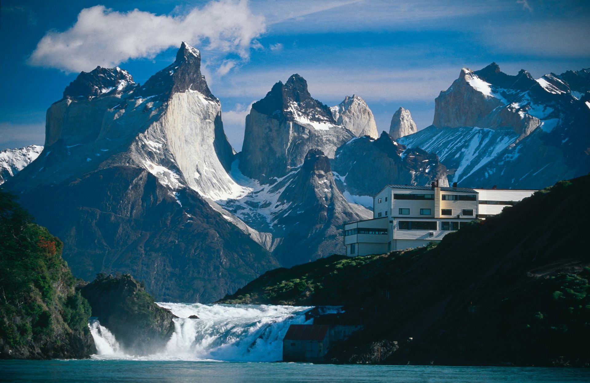 A waterfall with mountains in the background and a building in the foreground