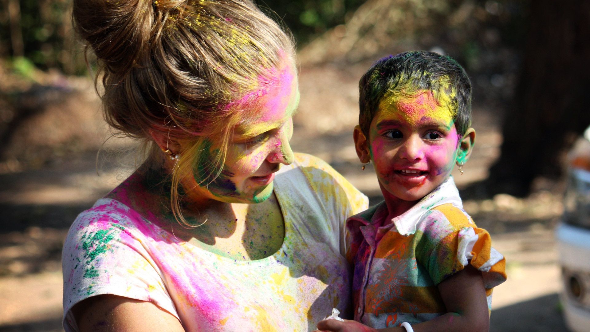 A woman is holding a child with holi paint on their faces.