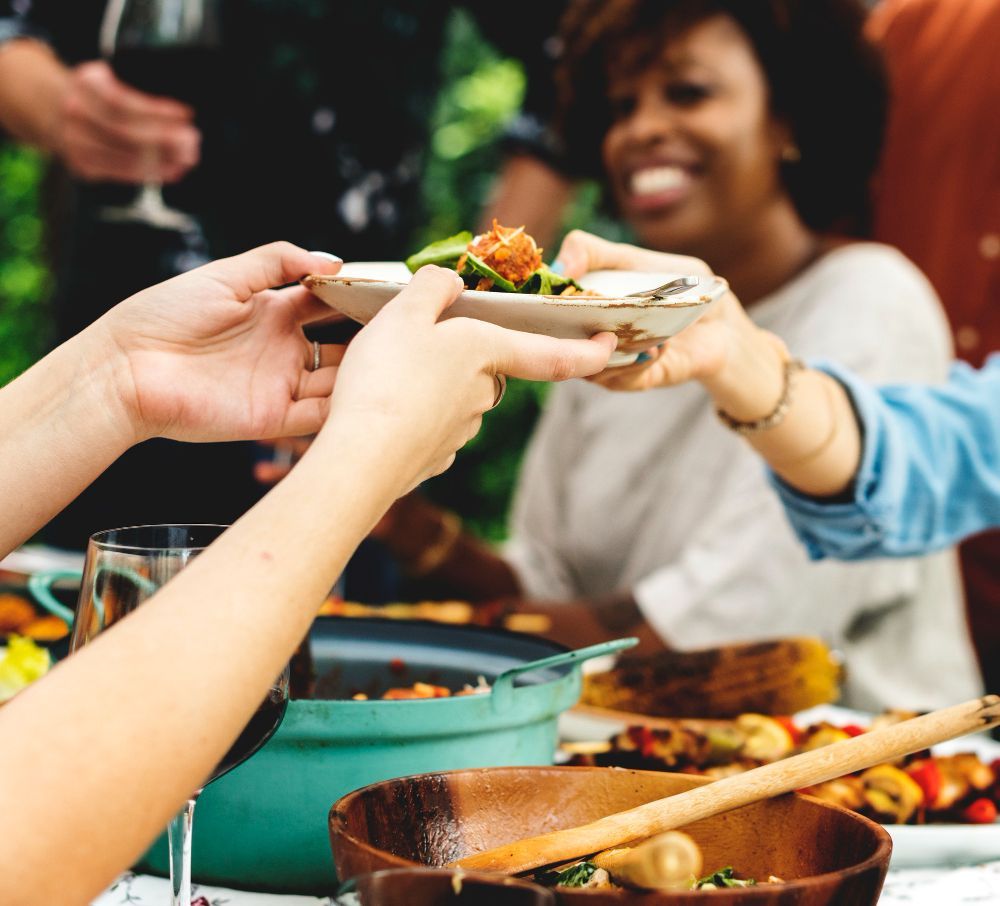 A group of people are sitting at a table eating Jamaican food and drinking wine.