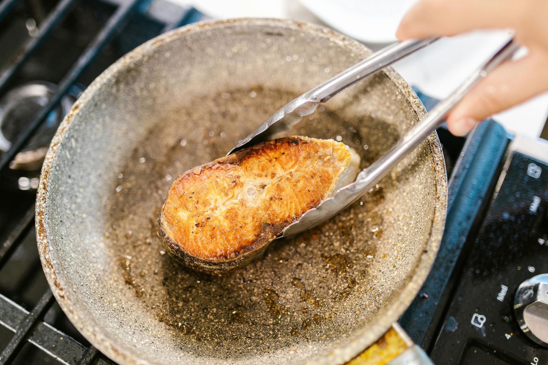 A piece of meat is being cooked in a pan with tongs.