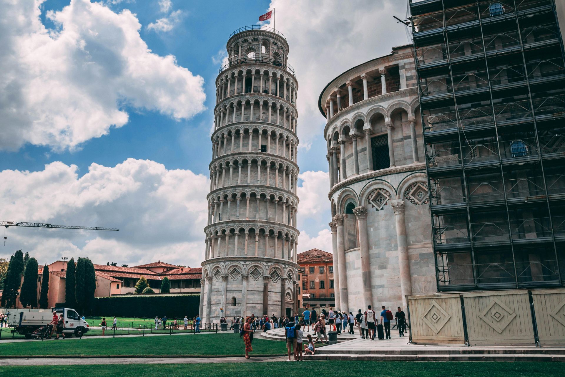 The leaning tower of Pisa is surrounded by scaffolding and people.