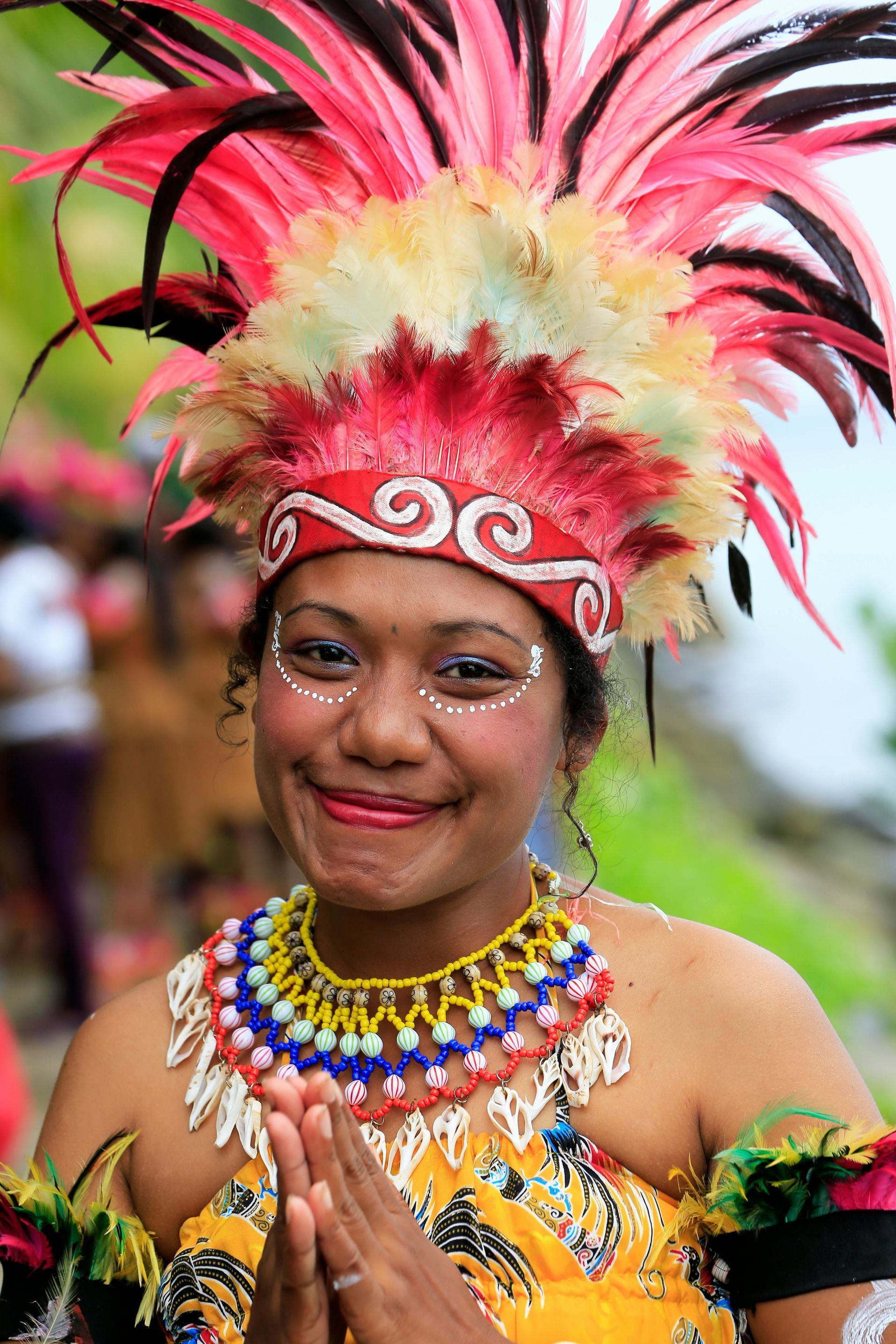 A woman wearing a feathered headdress and a necklace is smiling in South Pacific islands