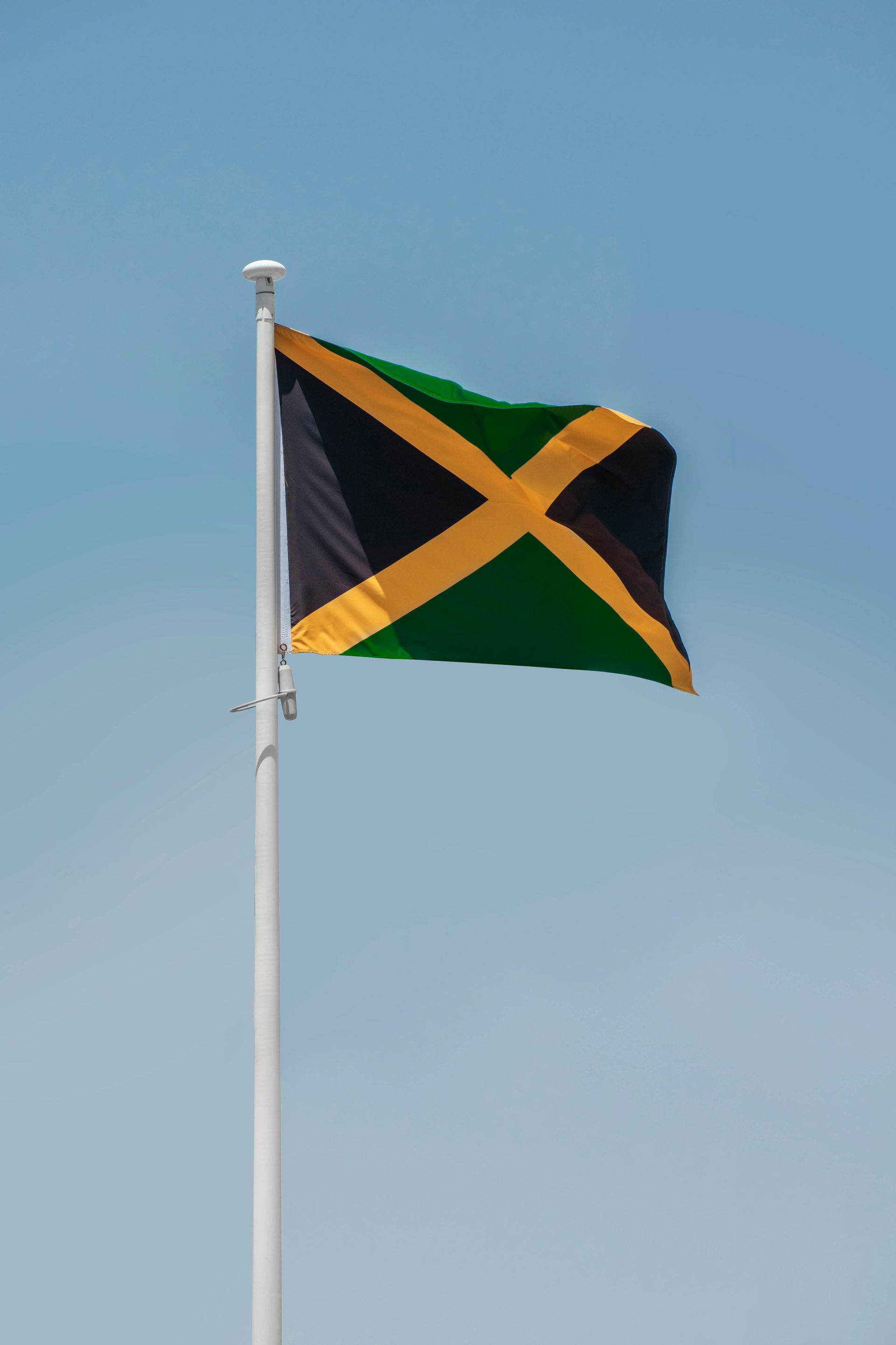A Jamaican flag is flying in the wind on a white pole