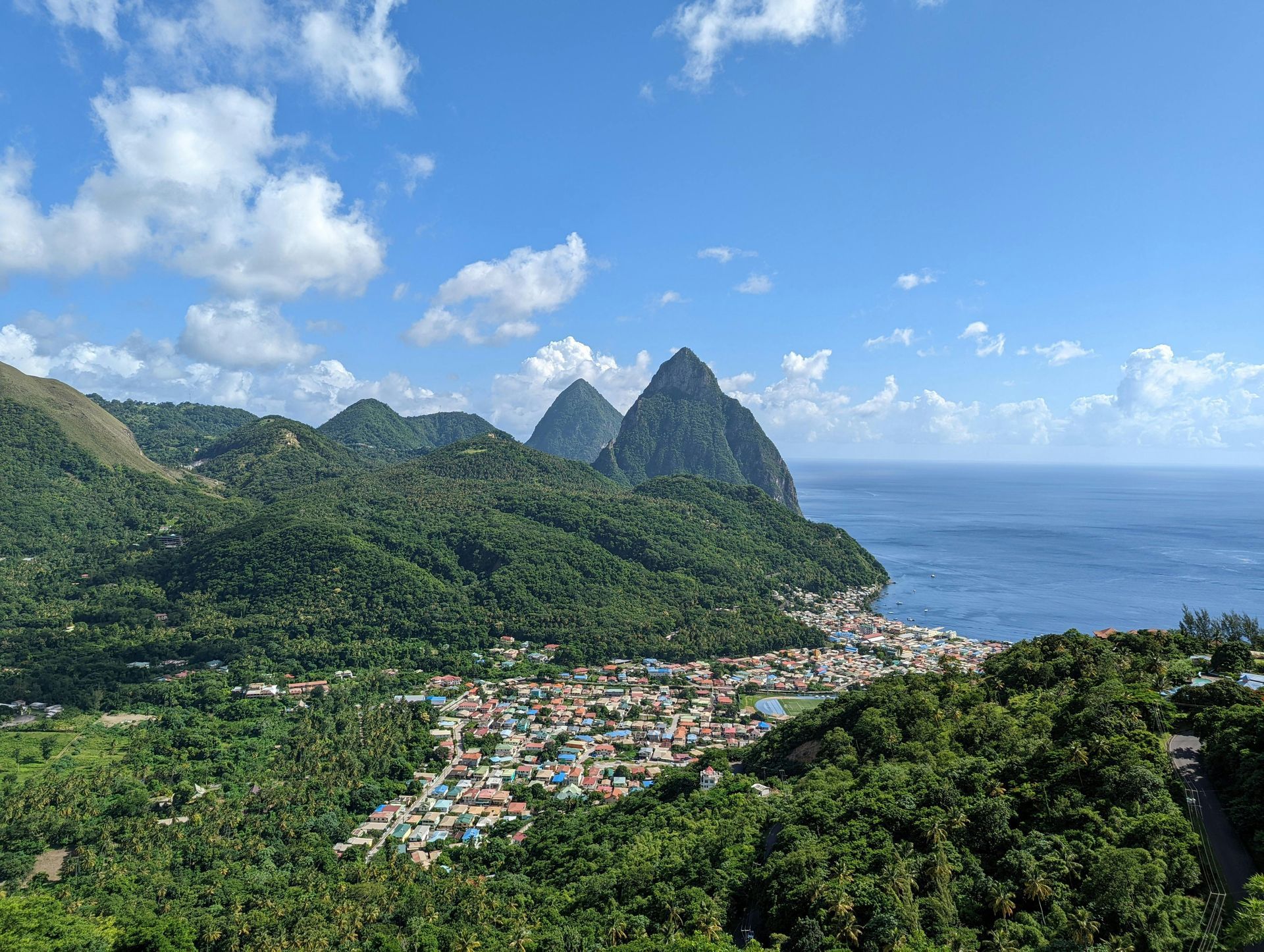 A view of a small town surrounded by mountains and trees overlooking the ocean.