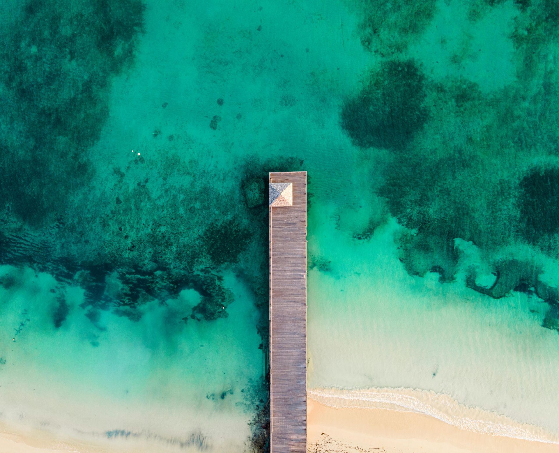An aerial view of a wooden pier in the middle of the ocean.