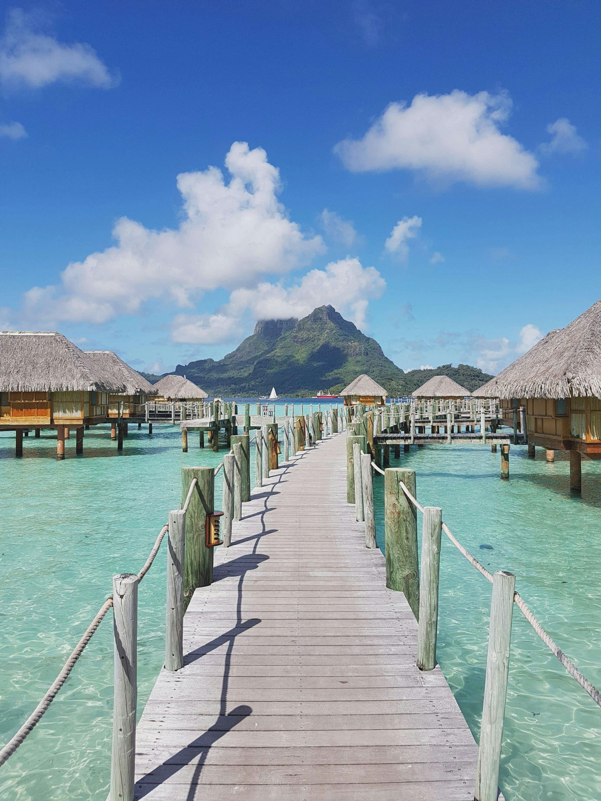 A wooden pier leading to a row of bungalows in the ocean.