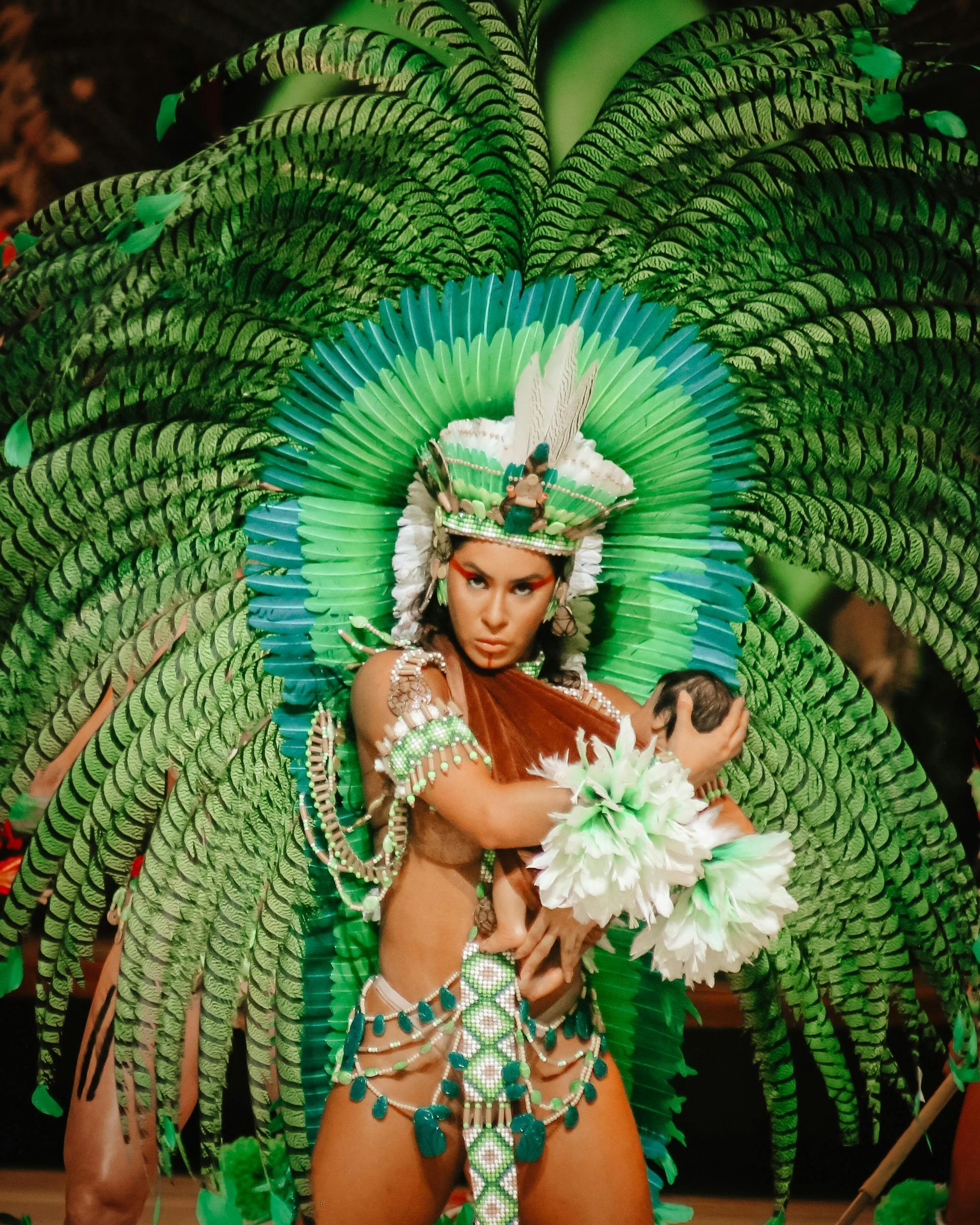 A woman in a carnival costume is holding a baby in her arms.