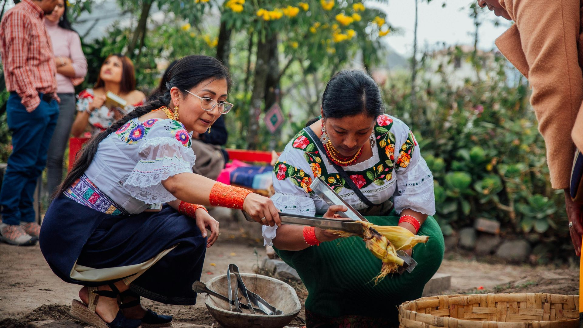 Two women are kneeling down in front of a bowl of food.