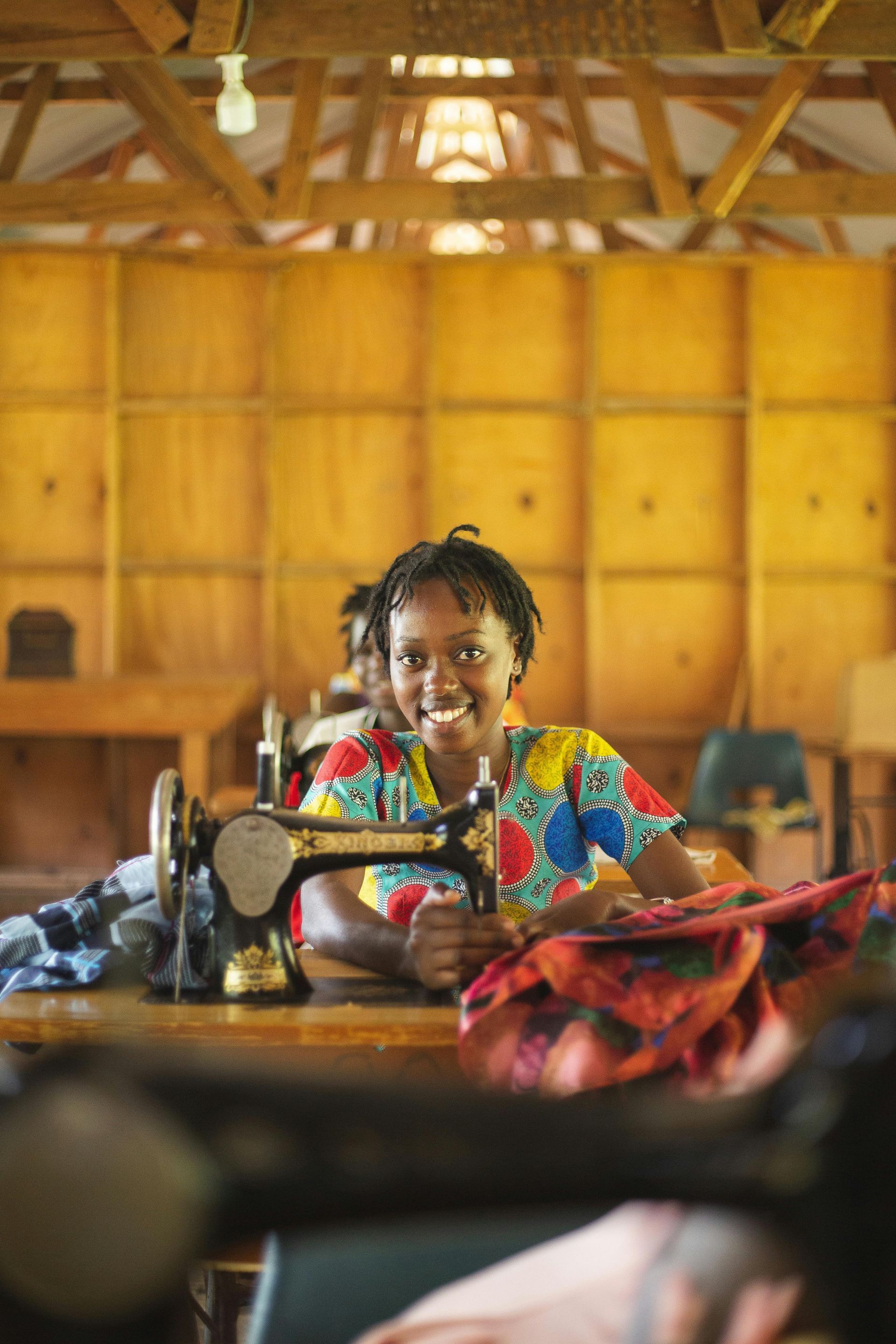 A woman is smiling while sitting at a table with a sewing machine.