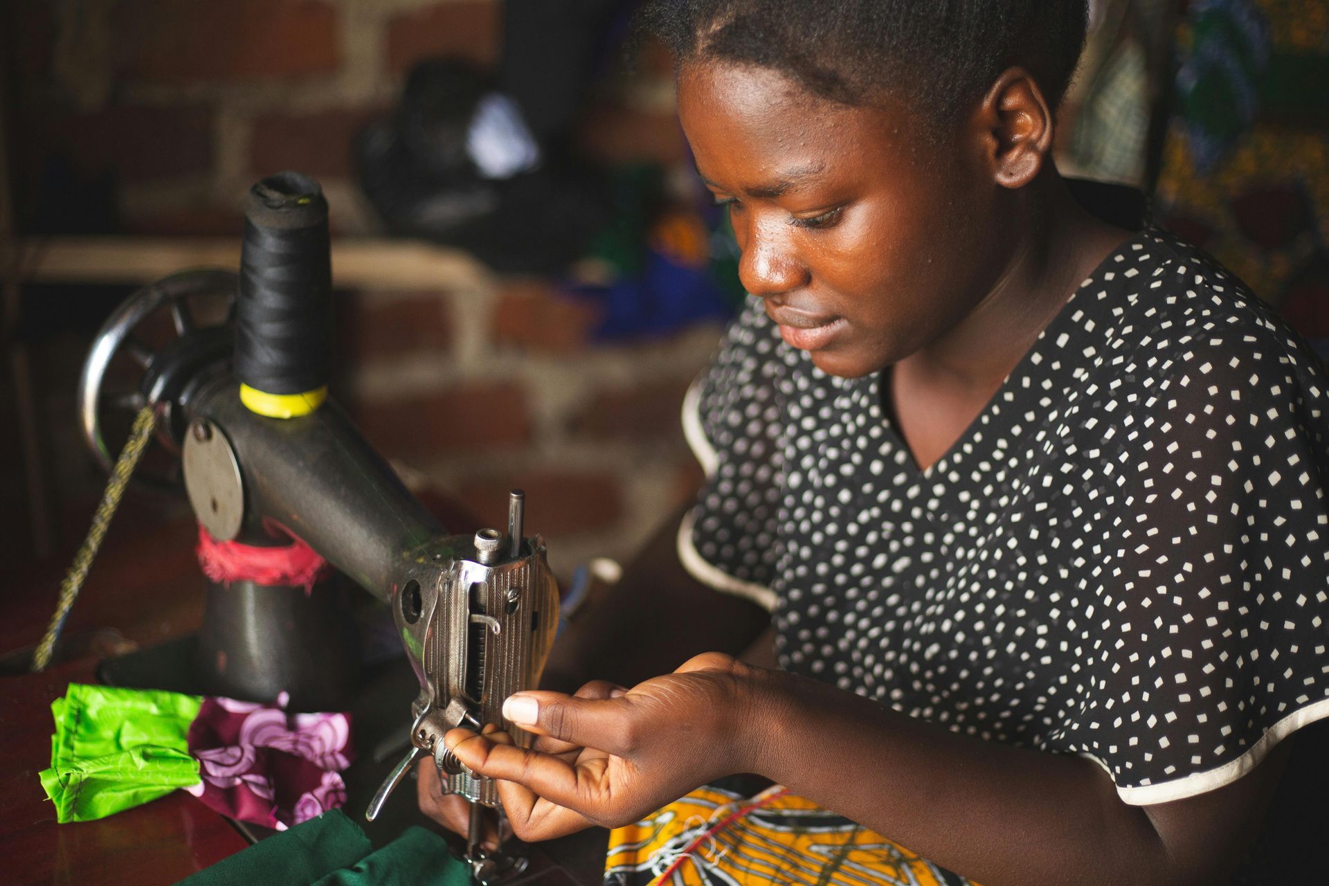 A woman is sitting at a table using a sewing machine making garments in Ugnada