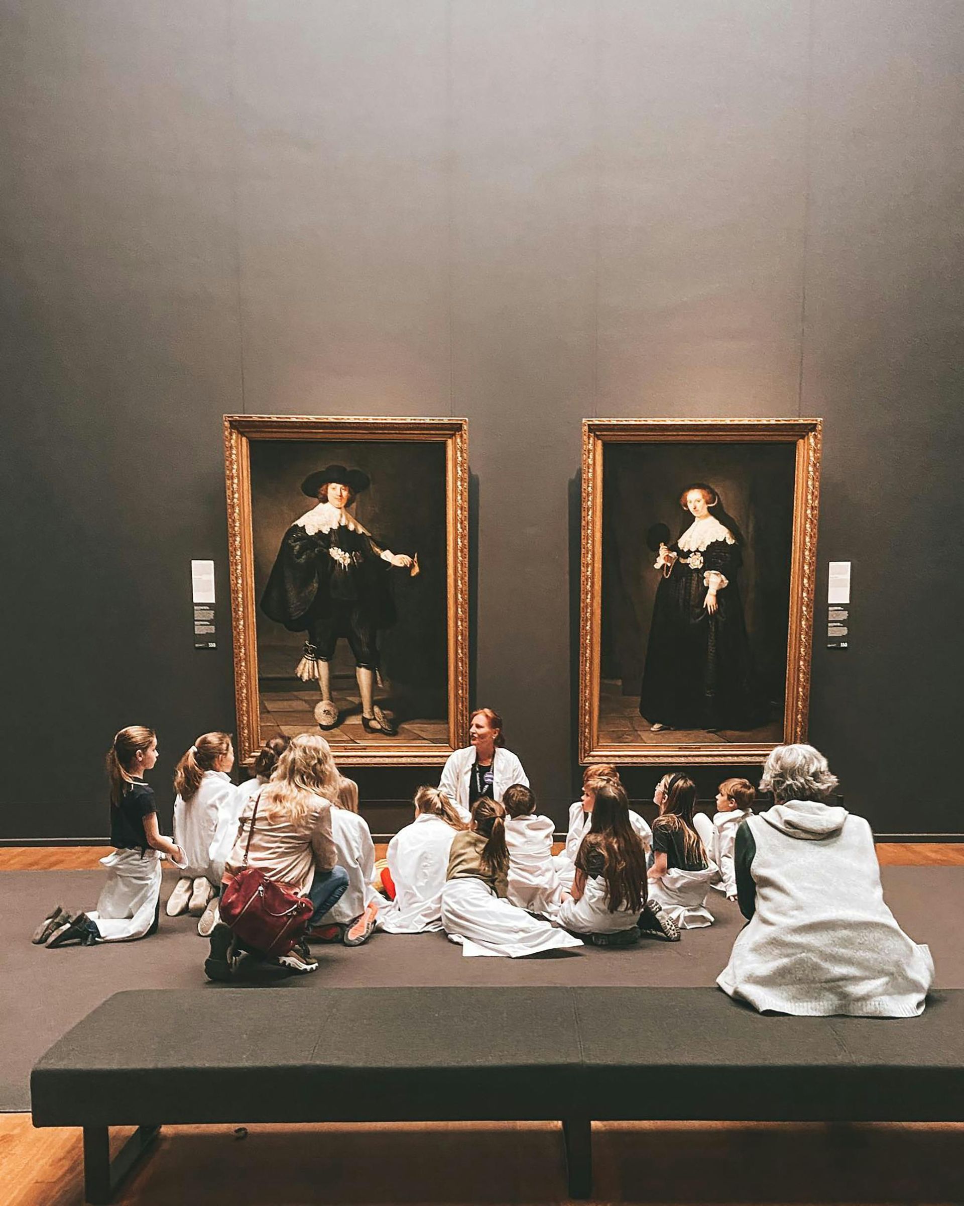 A group of people are sitting in front of two paintings in a museum.